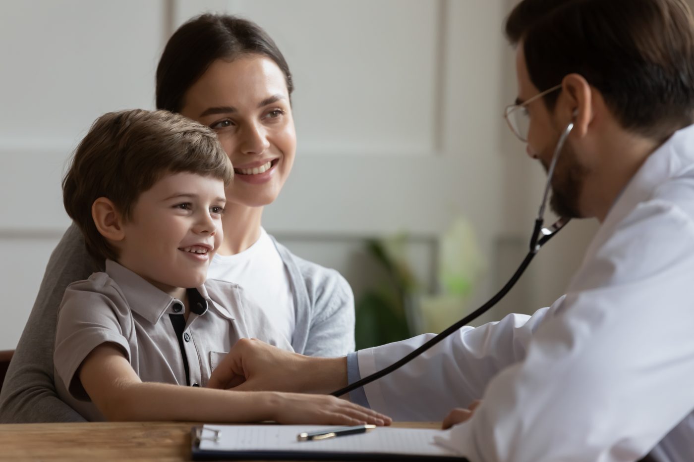 A GP examining a young boy with his mother beside him