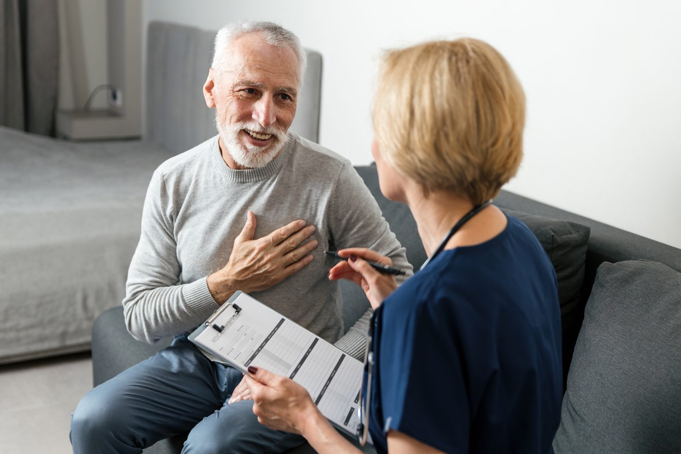 A GP talking with an older patient on the sofa at home during a home visit